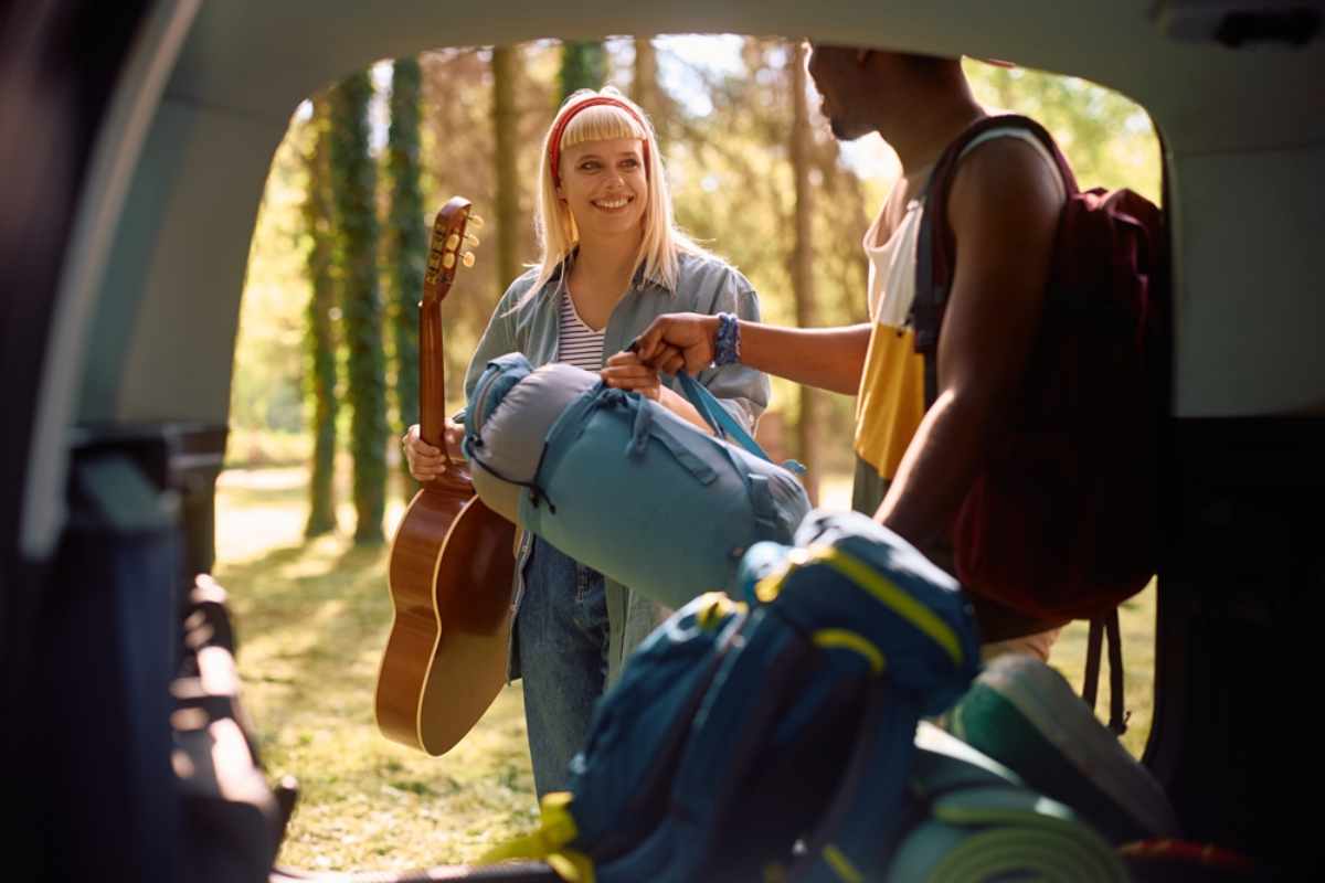 Twee jonge reizigers Twee jonge reizigers laden hun rugzakken bij de auto in een bos, klaar voor hun kampeertrip.