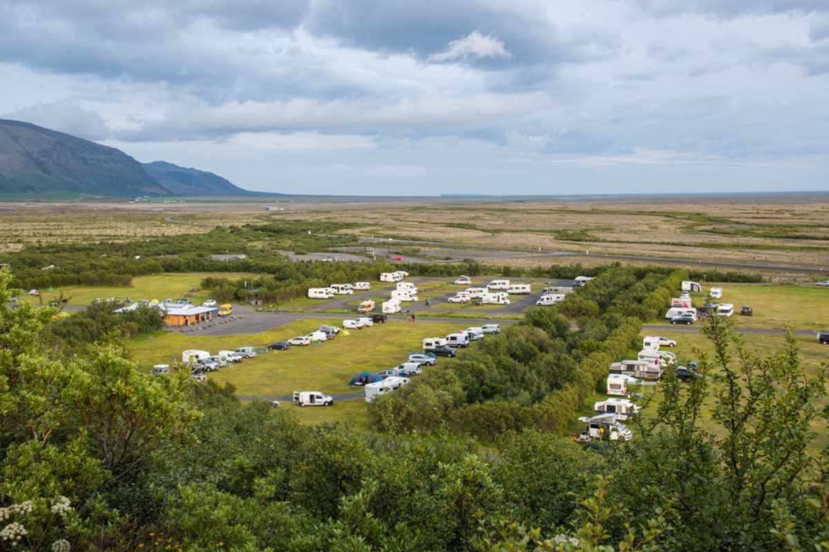 Grote IJslandse camping Grote IJslandse camping met campers en buscampers te midden van groen, met bergen en open vlaktes op de achtergrond.