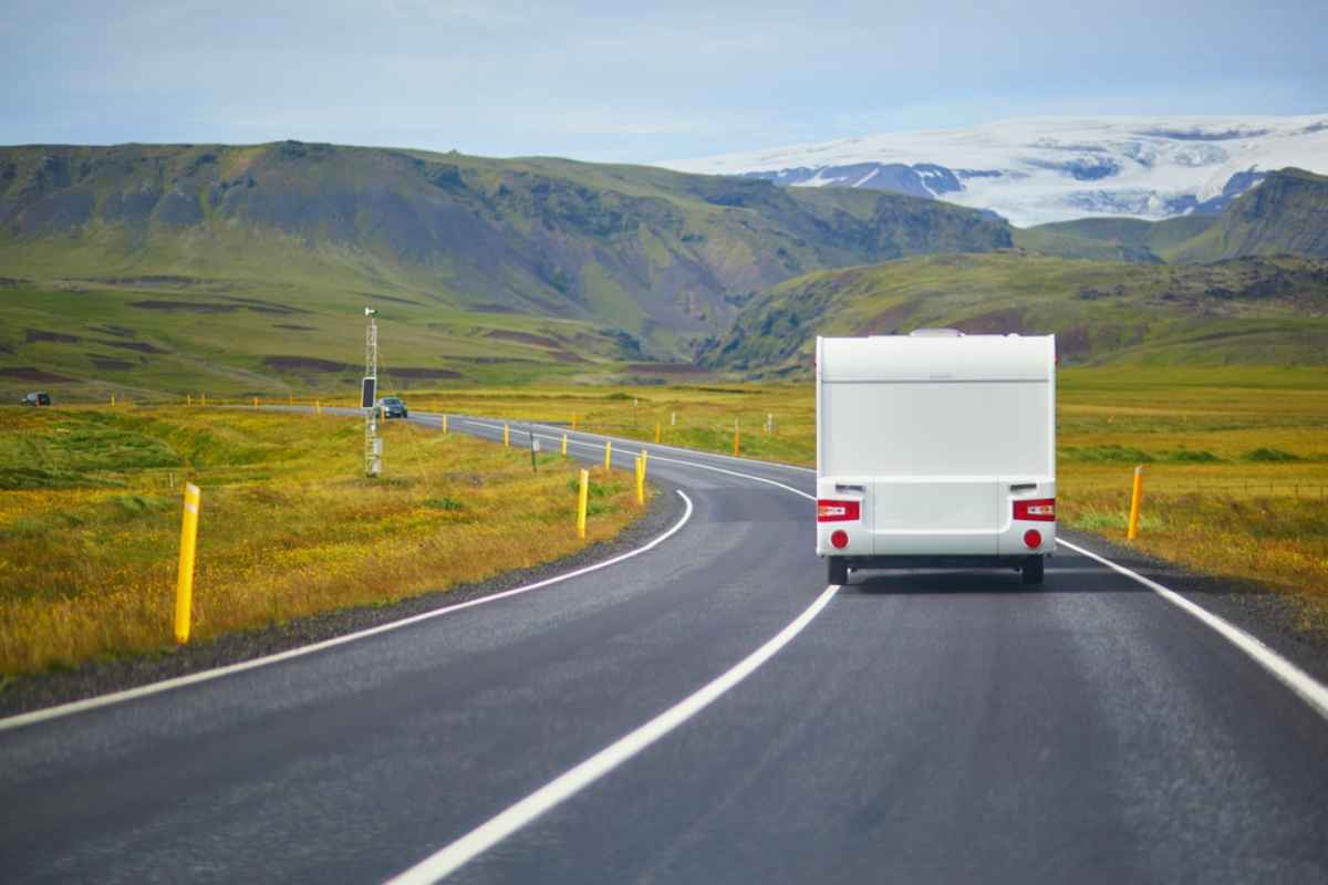 Een witte camper rijdt ontspannen over een heldere en kleurrijke strook van de IJslandse Ring Road.