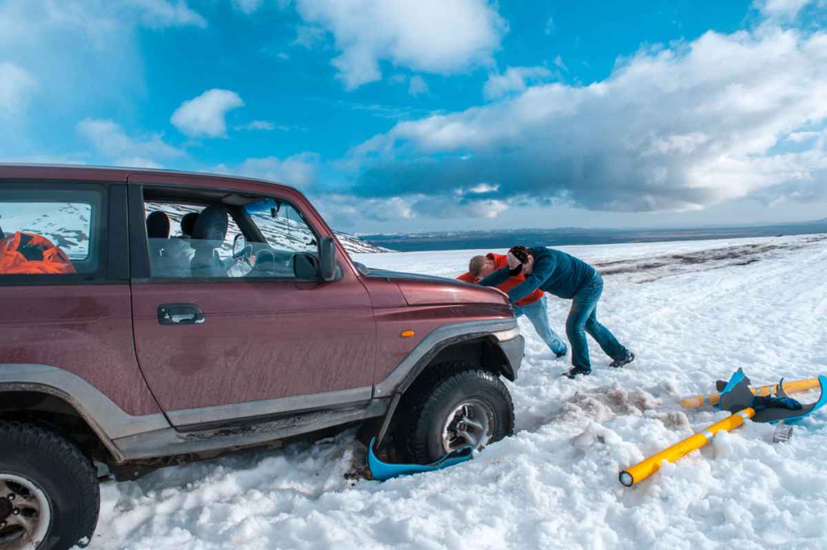 Een groep mannen probeert een 4x4-voertuig los te duwen dat vastzit in de sneeuw.