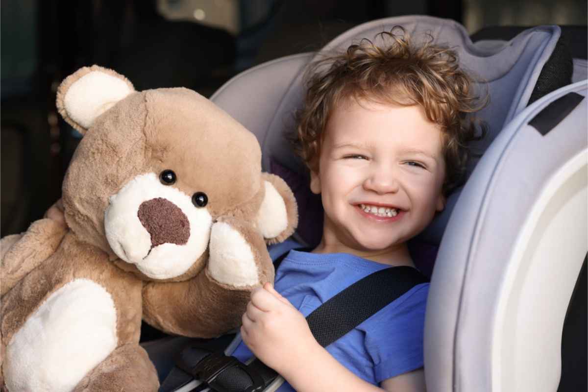 Vrolijk kind dat in zijn autostoeltje zit samen met een teddybeer